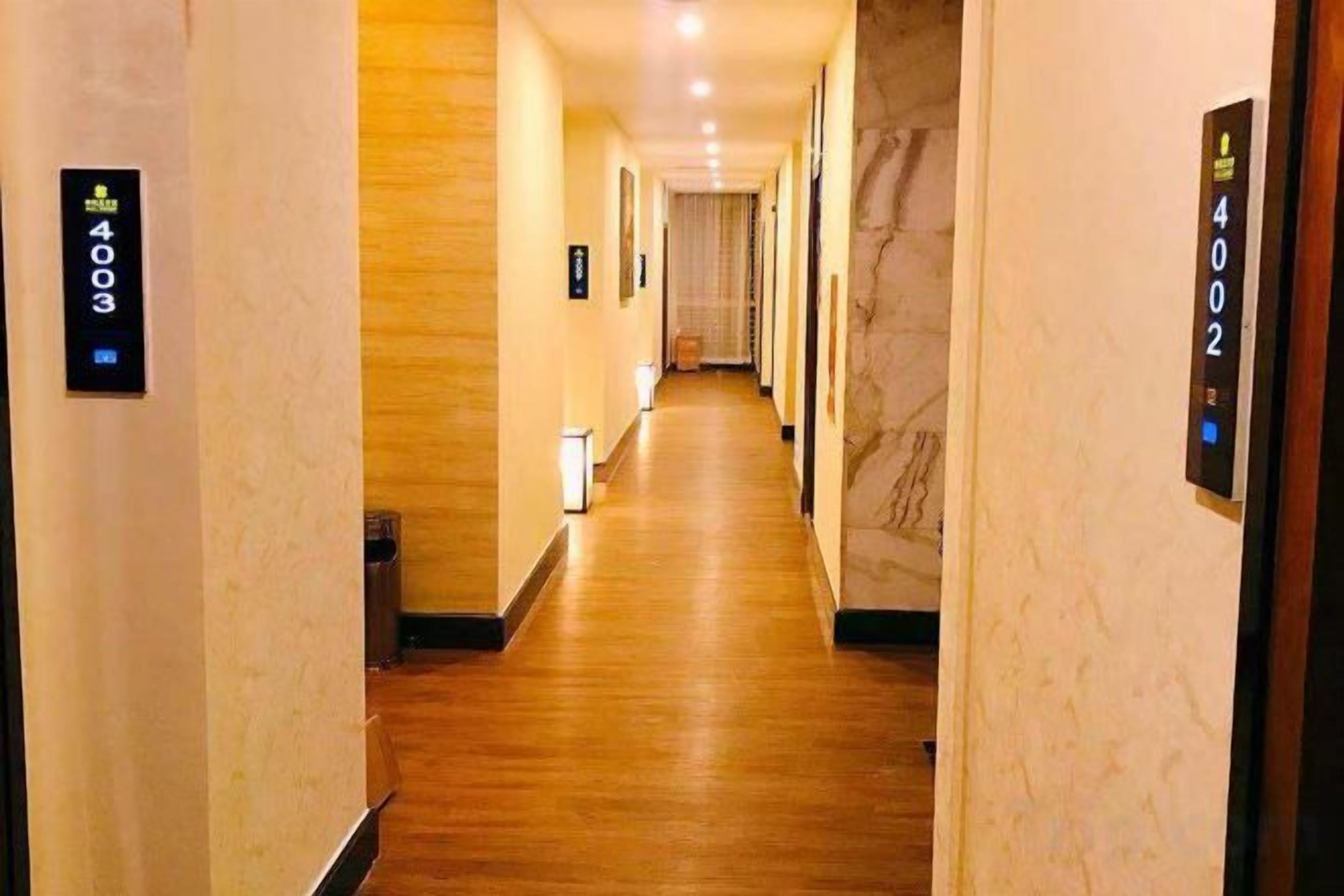 A hotel corridor with a wooden floor, marble walls, and numbered doors.