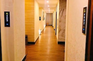 Un pasillo de hotel con suelo de madera, paredes de mármol y puertas numeradas.