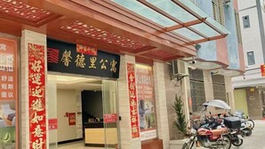 A hotel entrance with a reception desk, a glass door, and a red banner with Chinese characters. There are motorcycles parked outside. - Xindeli Apartment (Lufeng)