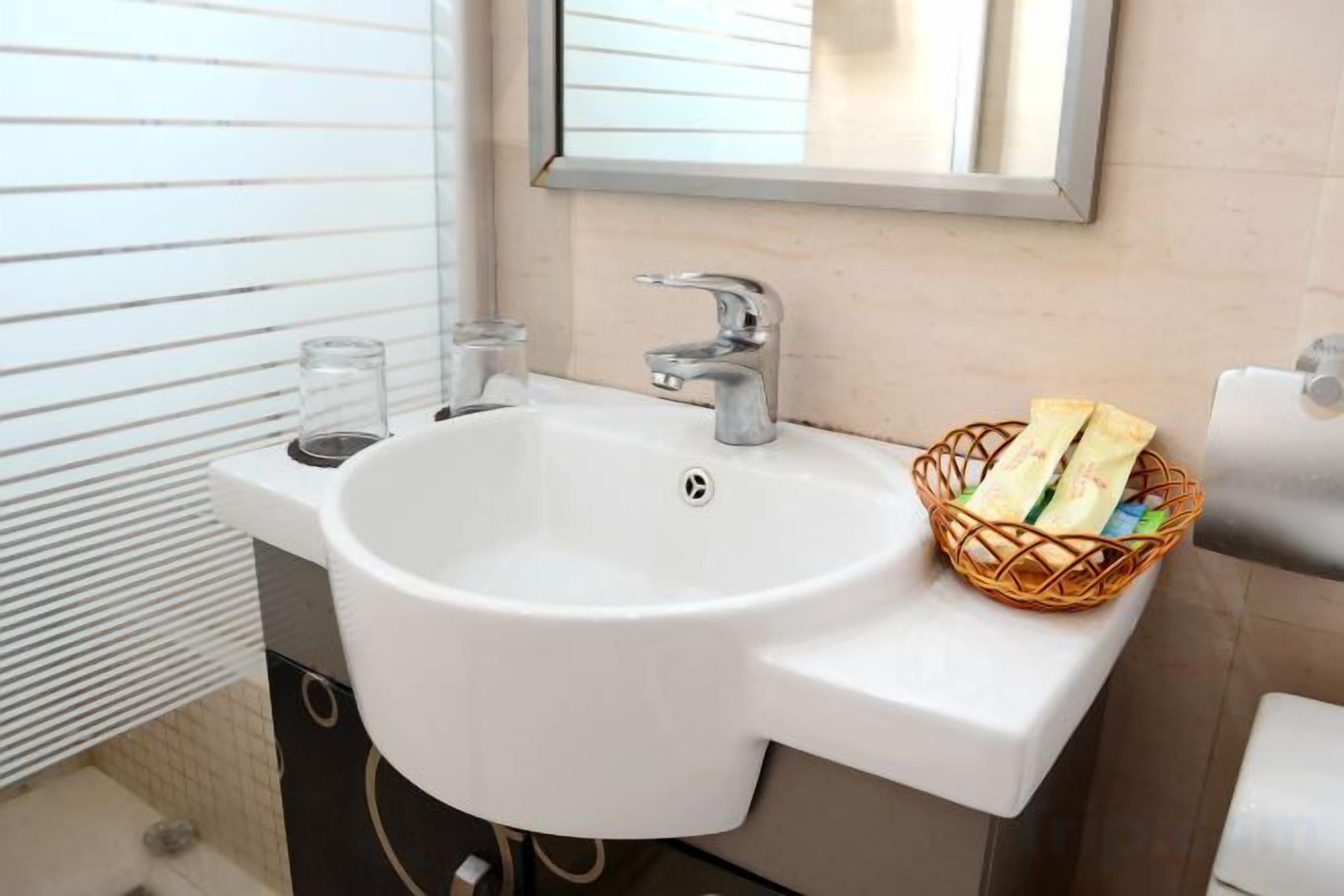 Un baño con un lavabo blanco, un espejo y una cesta de artículos de aseo.