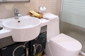 A bathroom with a white sink, a toilet, and a shower area. - Xindeli Apartment (Lufeng)
