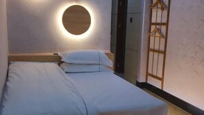 A neatly made bed with white linens, a round wall-mounted light fixture above it, and a wooden wardrobe with a hanging rack to the right. - Xindeli Apartment (Lufeng)