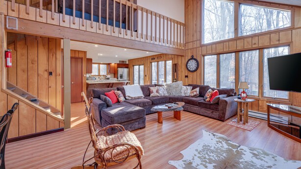 A spacious loft-style living area with a large sectional sofa, a wooden staircase, and a balcony. - Large rustic style home in gated community: Fire Pit - Lake - Beach - pools! (Gouldsboro)