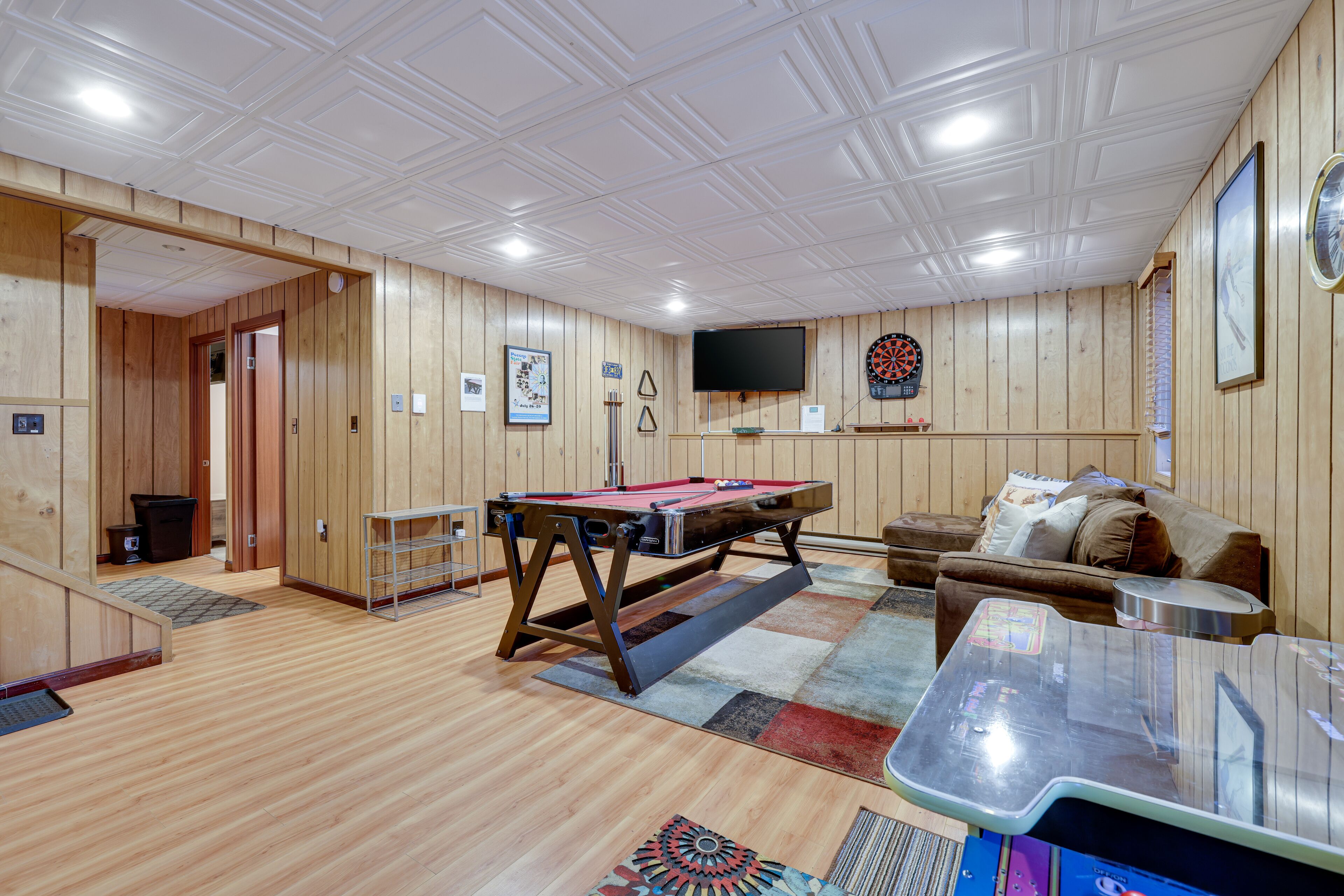 Una habitación con paredes y techo de madera, mesa de billar, dardos, televisor y sofá.