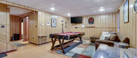 Una habitación con paredes y techo de madera, mesa de billar, dardos, televisor y sofá.