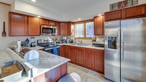 A modern kitchen with wooden cabinets, stainless steel appliances, a granite countertop, and a built-in island. - Large rustic style home in gated community: Fire Pit - Lake - Beach - pools! (Gouldsboro)