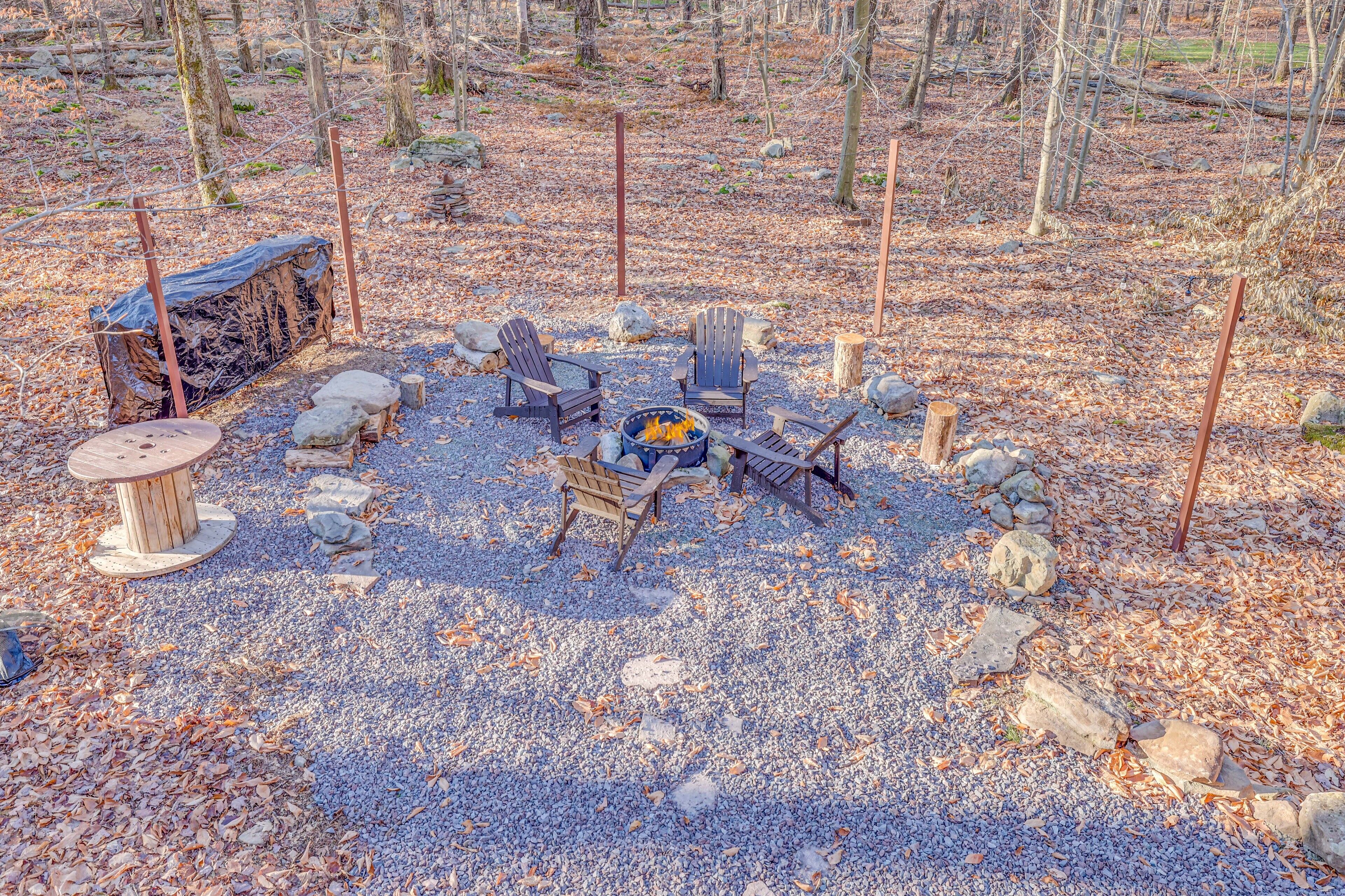 A rustic outdoor seating area with Adirondack chairs, a fire pit, and a wooden table.