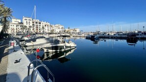 A marina with boats docked, a building with balconies, and palm trees. - Casares Beach Doña Julia Golf Apartment With Private Garden Direct Pool Access (Casares)