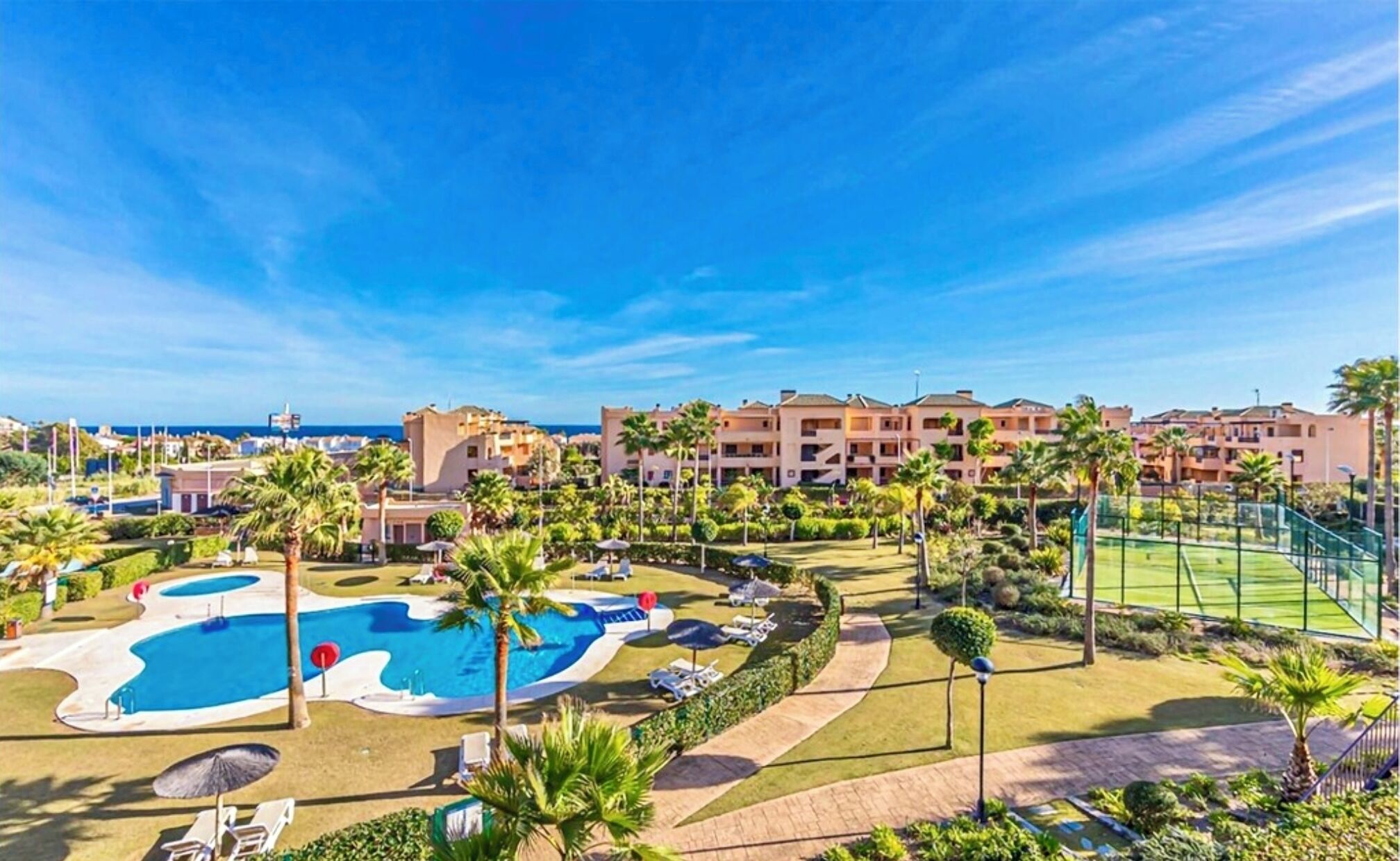 A resort with a pool area, palm trees, and a view of the sea.