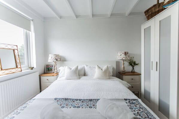 Quarto com cama, mesas de cabeceira, penteadeira e janela.