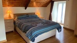 Une chambre avec un plafond en bois, un lit recouvert d’une courtepointe à rayures, deux lampes de chevet et une fenêtre avec des rideaux.