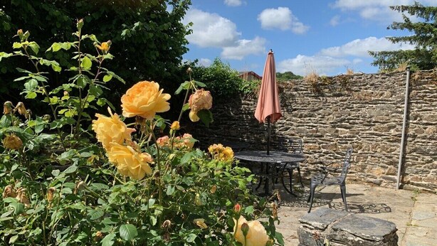 Un mur de pierres, une table avec des chaises et un parasol rose, le tout dans un cadre de jardin.