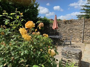 A stone wall, a table with chairs, and a pink umbrella in a garden setting. - A wonderful stone cottage sleeps up to 5, is set in a quiet lane yet near to shops, lake etc. (Caurel)
