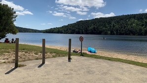 Une vue sur le lac, avec une plage de sable, une tente et un panneau indiquant qu’il est interdit de se baigner.