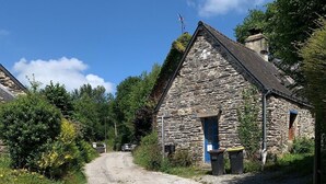 Un bâtiment en pierre avec une porte bleue, un chemin de gravier et de la verdure tout autour.