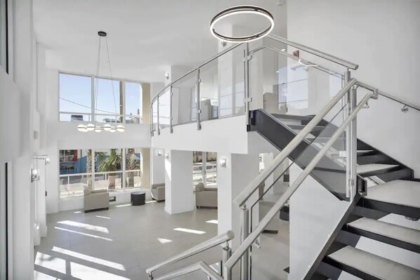 Un interior moderno con una escalera de cristal, ventanas amplias y un techo alto.