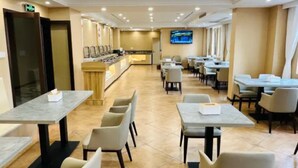Ein Hotel-Essbereich mit mehreren Tischen und Stühlen, einer Rezeption und einem Fernsehbildschirm.
