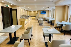 Un comedor de hotel con varias mesas y sillas, una recepción y una pantalla de televisión.