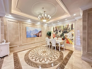 A luxurious dining room with a large chandelier, a dining table with white chairs, and a decorative floor pattern.