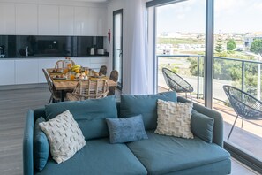 Un salon moderne avec un canapé de couleur turquoise, une table à manger où sont disposés des aliments pour le petit-déjeuner, et une cuisine en arrière-plan.