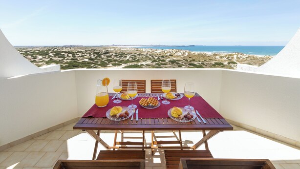 A dining table with plates, cutlery, and glasses, set on a balcony with a view of the beach and ocean. - Baleal Balcony - Sea & Beach view (Peniche)