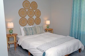A neatly made bed with a white duvet, two bedside tables with lamps, a wall with circular woven decorations, and a blue curtain.