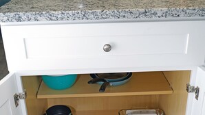 Une cuisine avec un plan de travail en granit, un meuble blanc doté d’un tiroir et une étagère en bois.