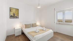 Une chambre à coucher avec un lit, des tables de chevet, une commode, une fenêtre et un tableau au mur.