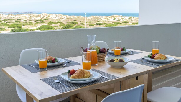 A breakfast table with plates of food, glasses of orange juice, and a basket of fruits. - Baleal Dream - front of the beach (Peniche)