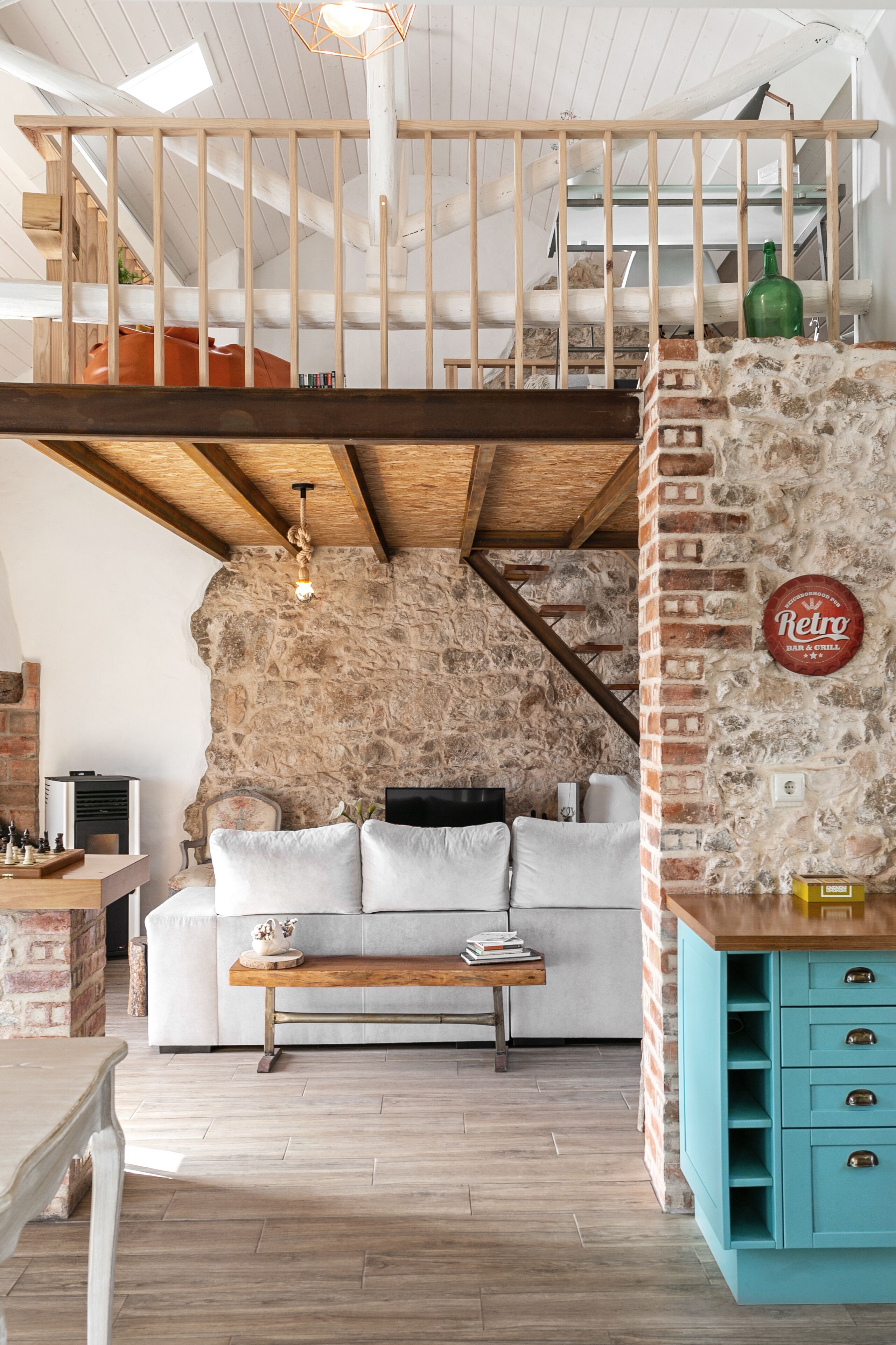 En stue i loftstil med synlige træbjælker, en stenvæg, en hvid sofa og et blå skab.