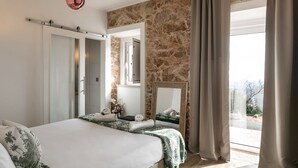 Un dormitorio con una cama grande, una pared de piedra, un espejo y vistas al exterior.