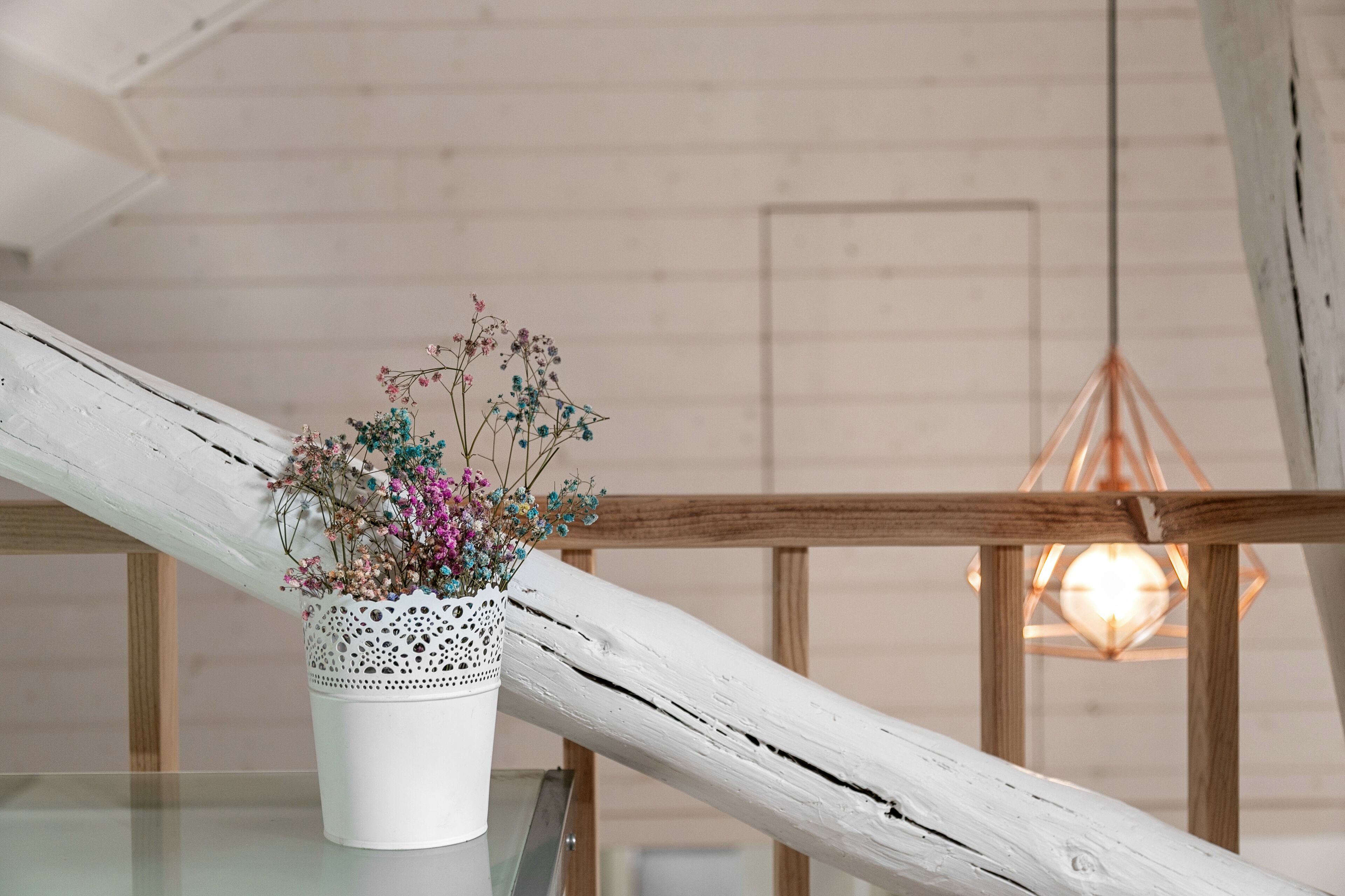 A white vase with flowers on a glass table.