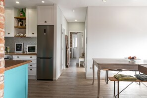 A modern kitchen with white cabinets, a stainless steel refrigerator, and a wooden countertop.