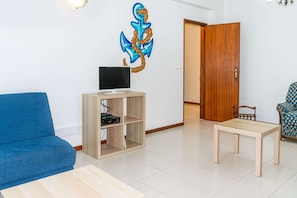 A living room with a blue sofa, a wooden TV stand, a wooden table, and a door leading to another room.
