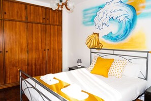 A hotel room with a bed, wooden wardrobe, and a wall mural of a wave.