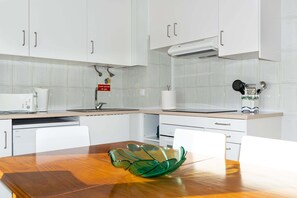 A modern kitchen with white cabinets, a wooden table, and a green glass bowl.