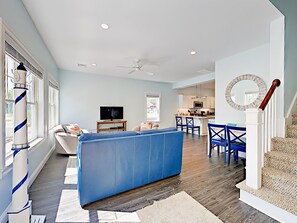 Un salón amplio con un sofá azul, una televisión y un comedor con sillas azules.