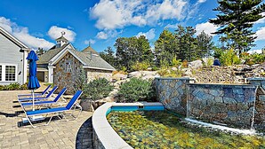 A swimming pool with a stone wall, lounge chairs, and a stone building. - Whale Song Accessible Cottage - Near Beaches w/ Resort-style Pool (Arundel)