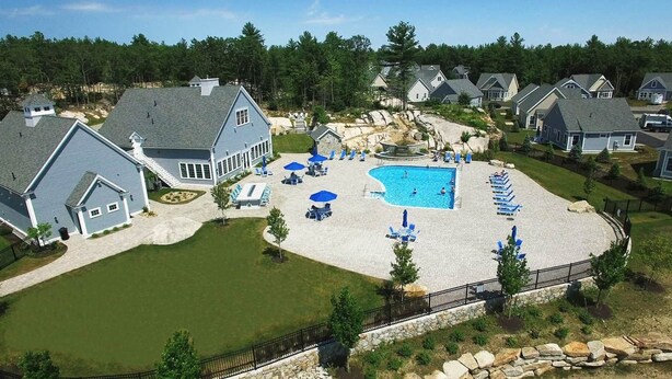 A residential area with a swimming pool surrounded by lounge chairs and umbrellas, a stone pathway, and houses with similar architecture. - Whale Song Accessible Cottage - Near Beaches w/ Resort-style Pool (Arundel)