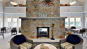 A spacious living area with a stone fireplace labeled "Relax," wicker furniture, and a view of the outdoors through large windows. - Whale Song Accessible Cottage - Near Beaches w/ Resort-style Pool (Arundel)