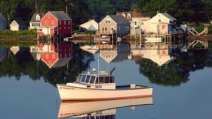 A boat docked near houses with reflections in calm water. - Whale Song Accessible Cottage - Near Beaches w/ Resort-style Pool (Arundel)