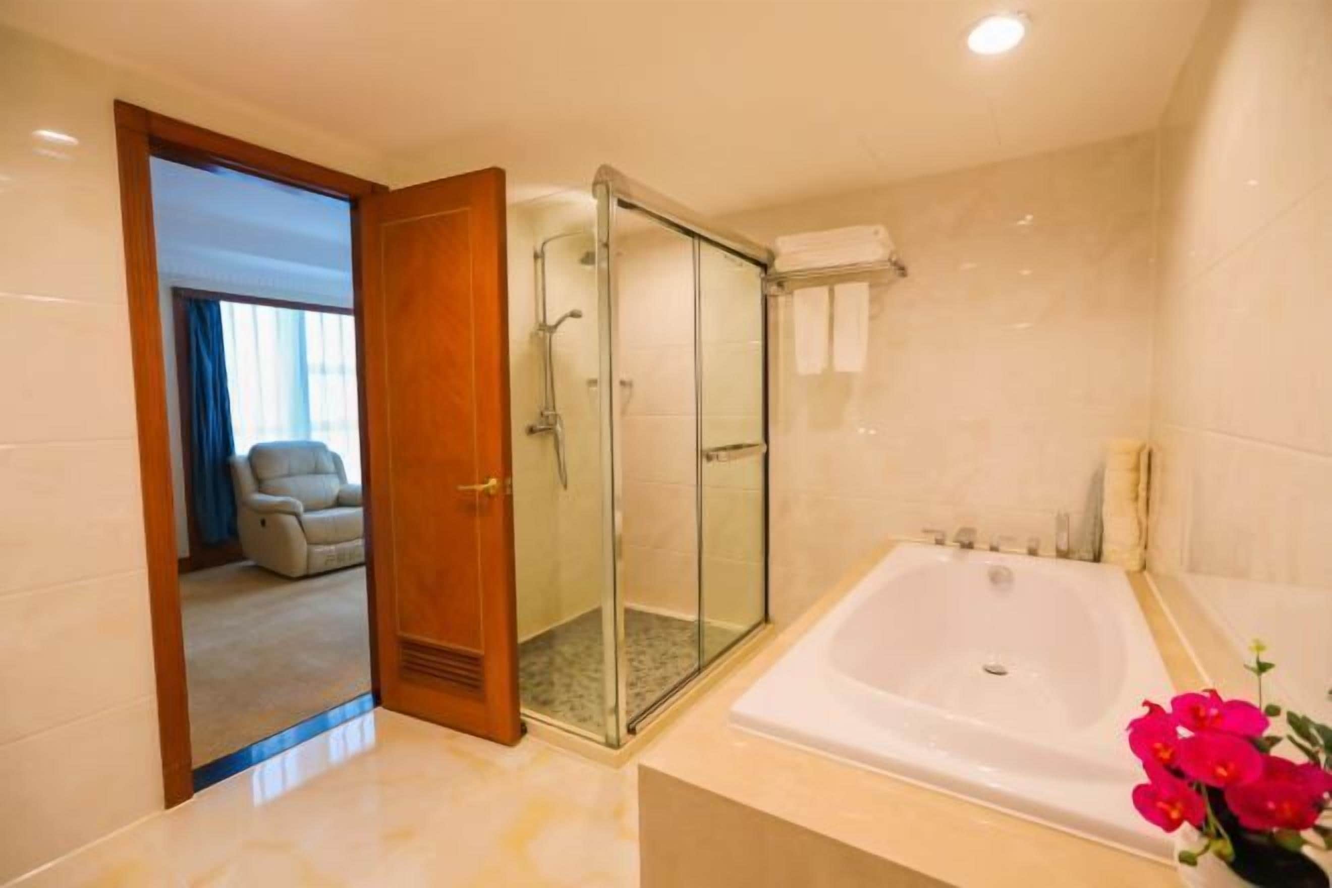 Un baño moderno con ducha de vidrio, una bañera amplia y una puerta visible que da a una sala de estar con sofá.