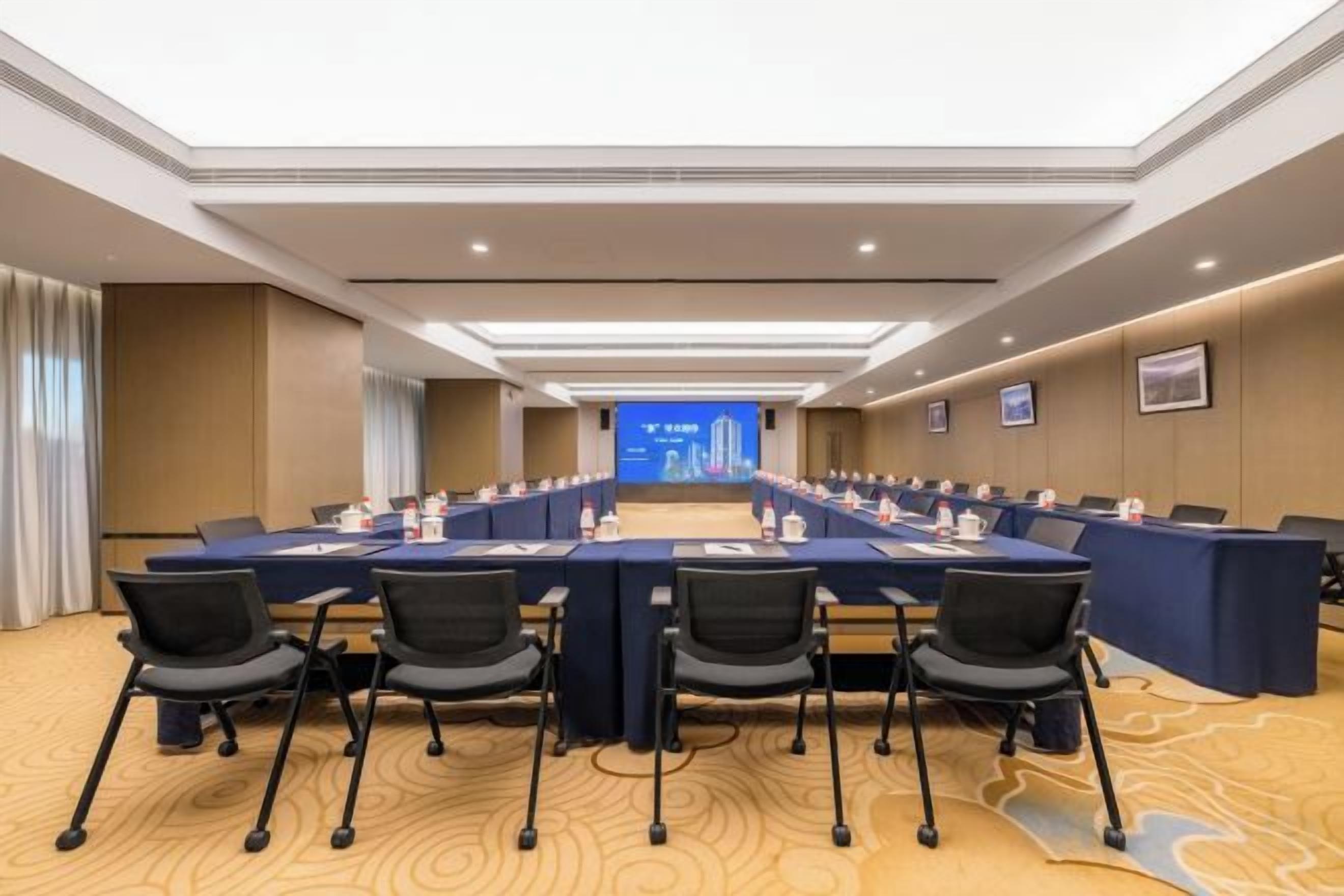 A conference room with a long table, multiple chairs, and a presentation screen at the front.