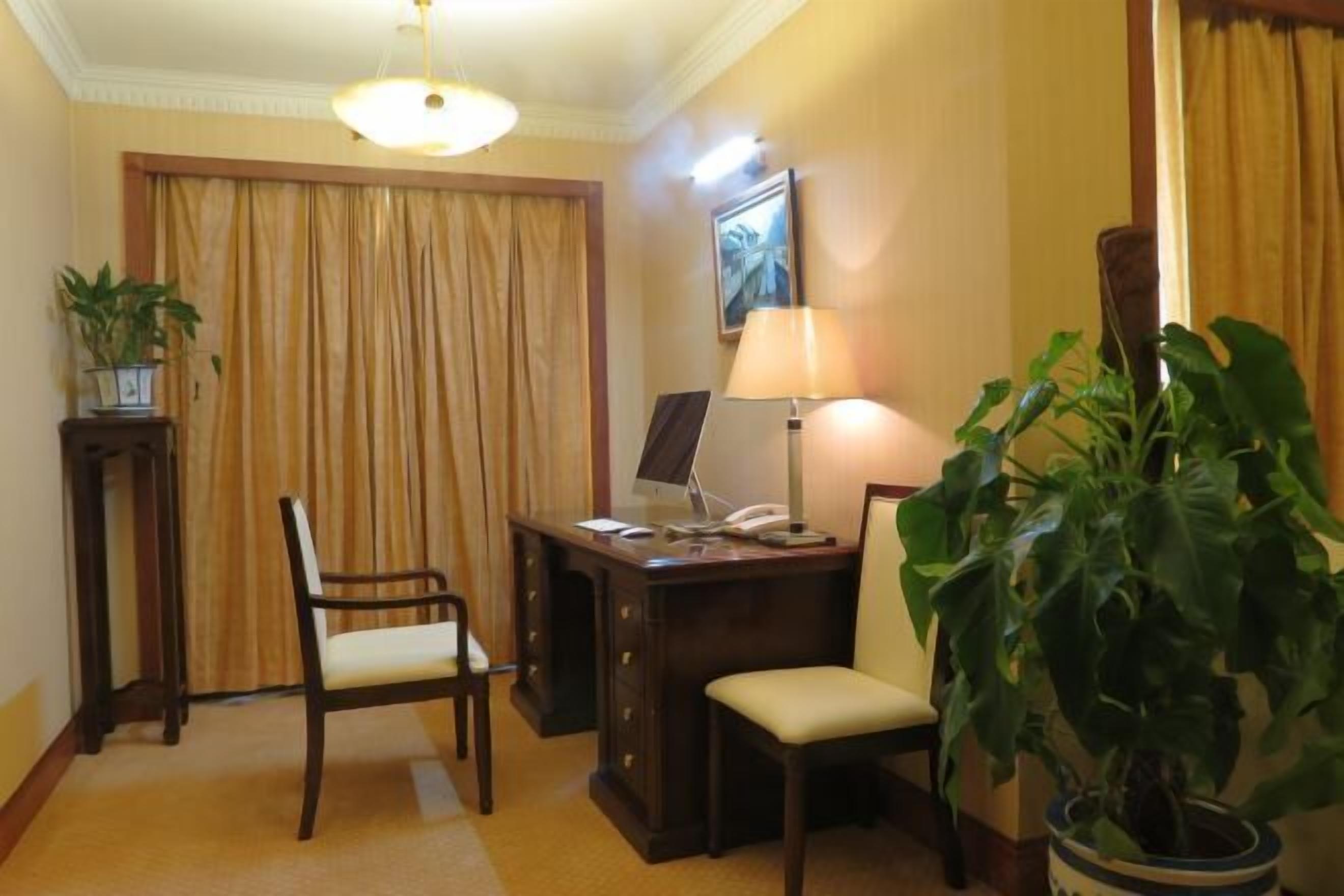 Hotelkamer met een bureau, twee stoelen, een lamp, een potplant en een raam met gordijnen.