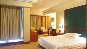 A hotel room with a bed, a desk with a chair, a lamp, and a window with curtains.