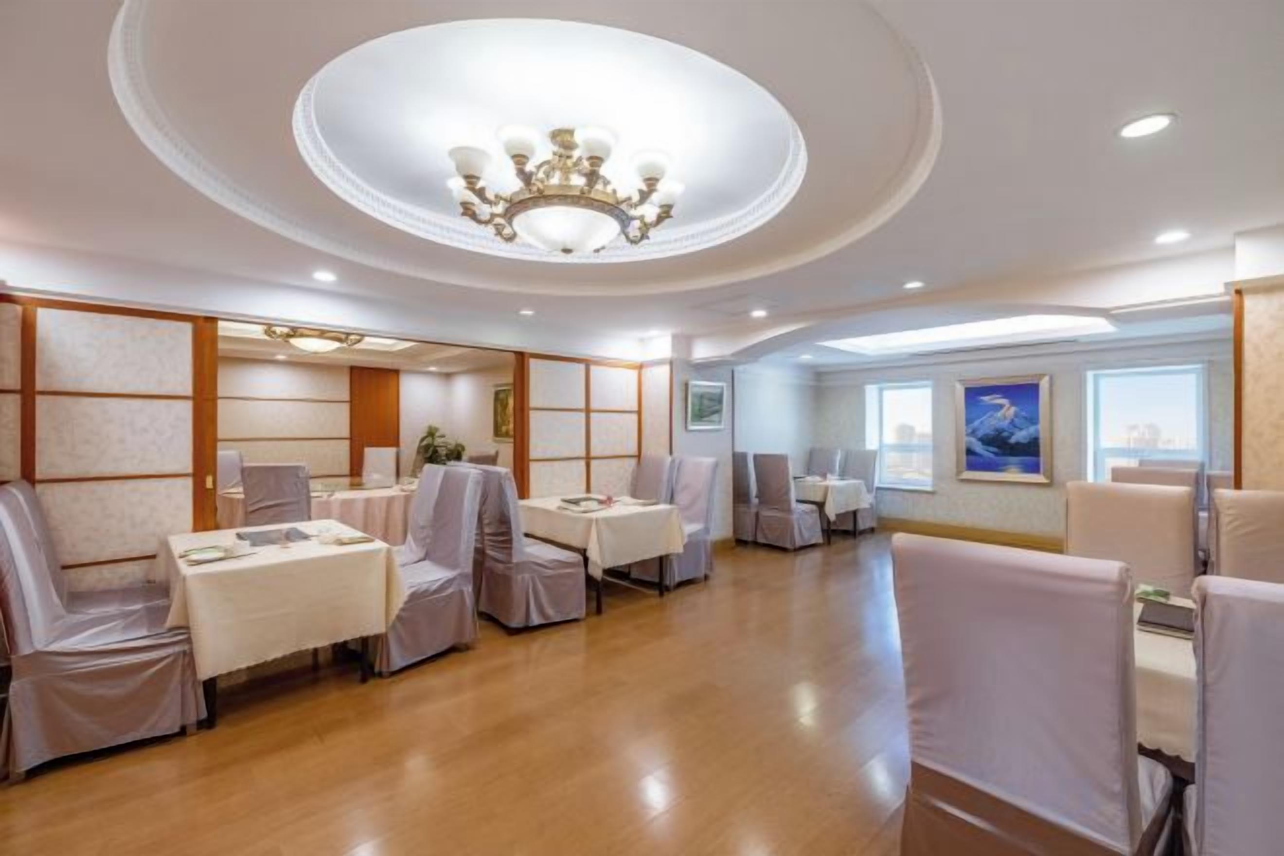 A hotel dining area with round tables, chairs, and a chandelier.