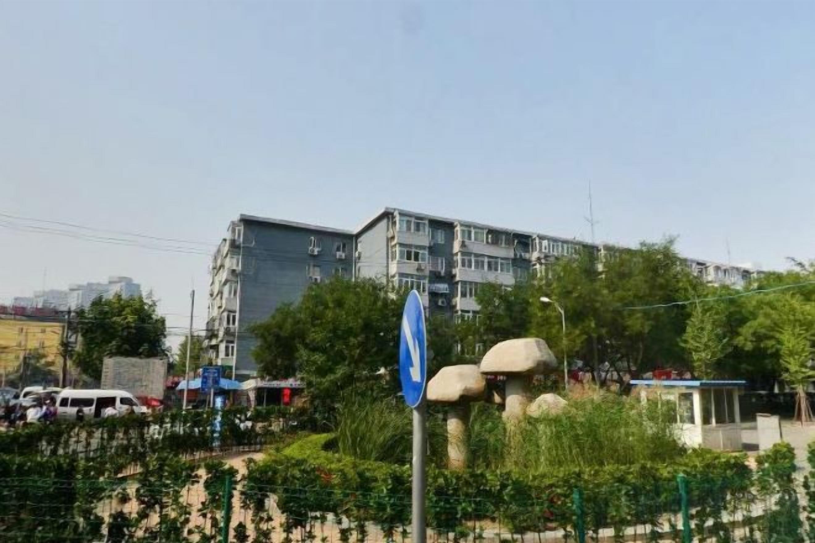 A multi-story building with a blue sign, surrounded by greenery and a fence.