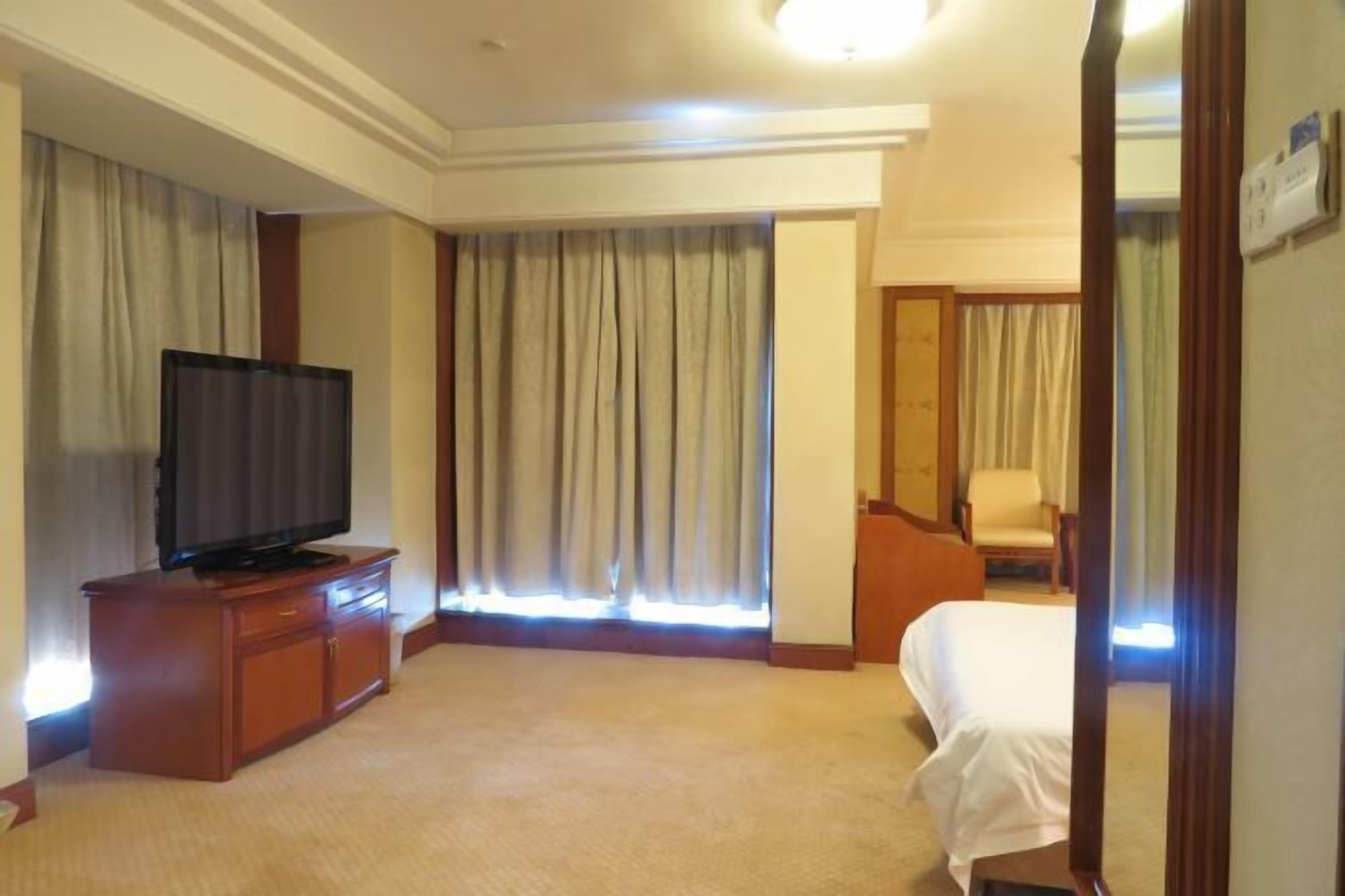 Een hotelkamer met een bed, een televisie op een houten kast, een stoel en een raam met gordijnen.