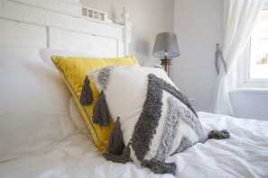 A bed with white bedding, a yellow pillow, and a gray and white patterned pillow. - Foresters Cottage (Worthing)