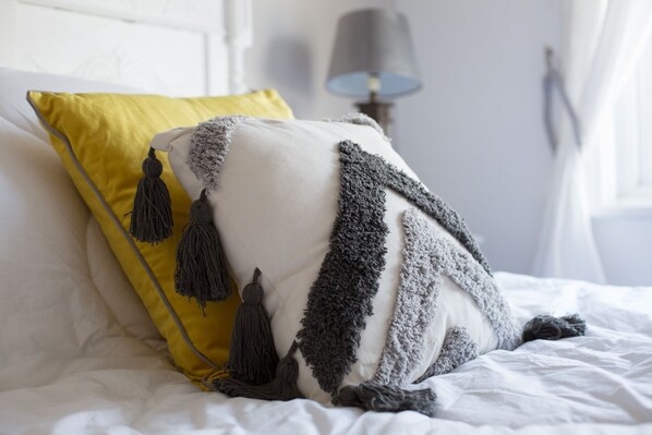 A bed with a white and yellow pillow, a grey blanket, and a lamp in the background. - Foresters Cottage (Worthing)